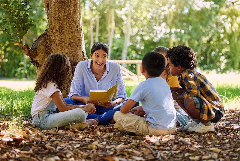 professora lendo para alunos em baixo da arvore