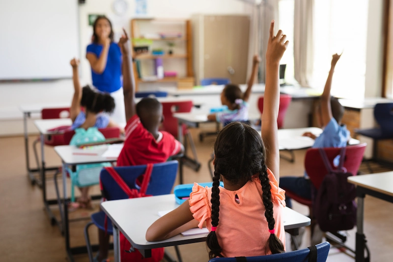 alunos em sala de aula levantando a mao