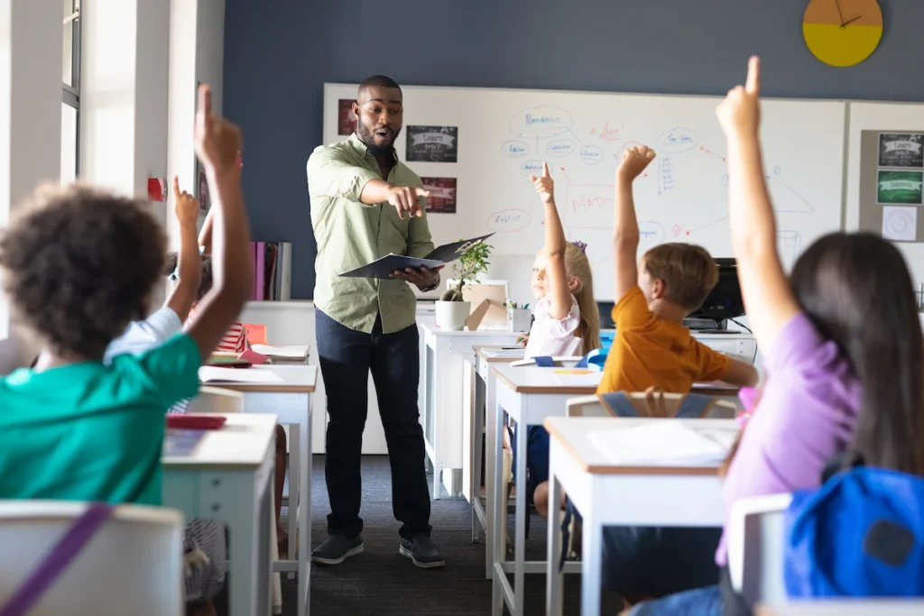 professor apontando para alunos com as maos levantadas em sala de aula